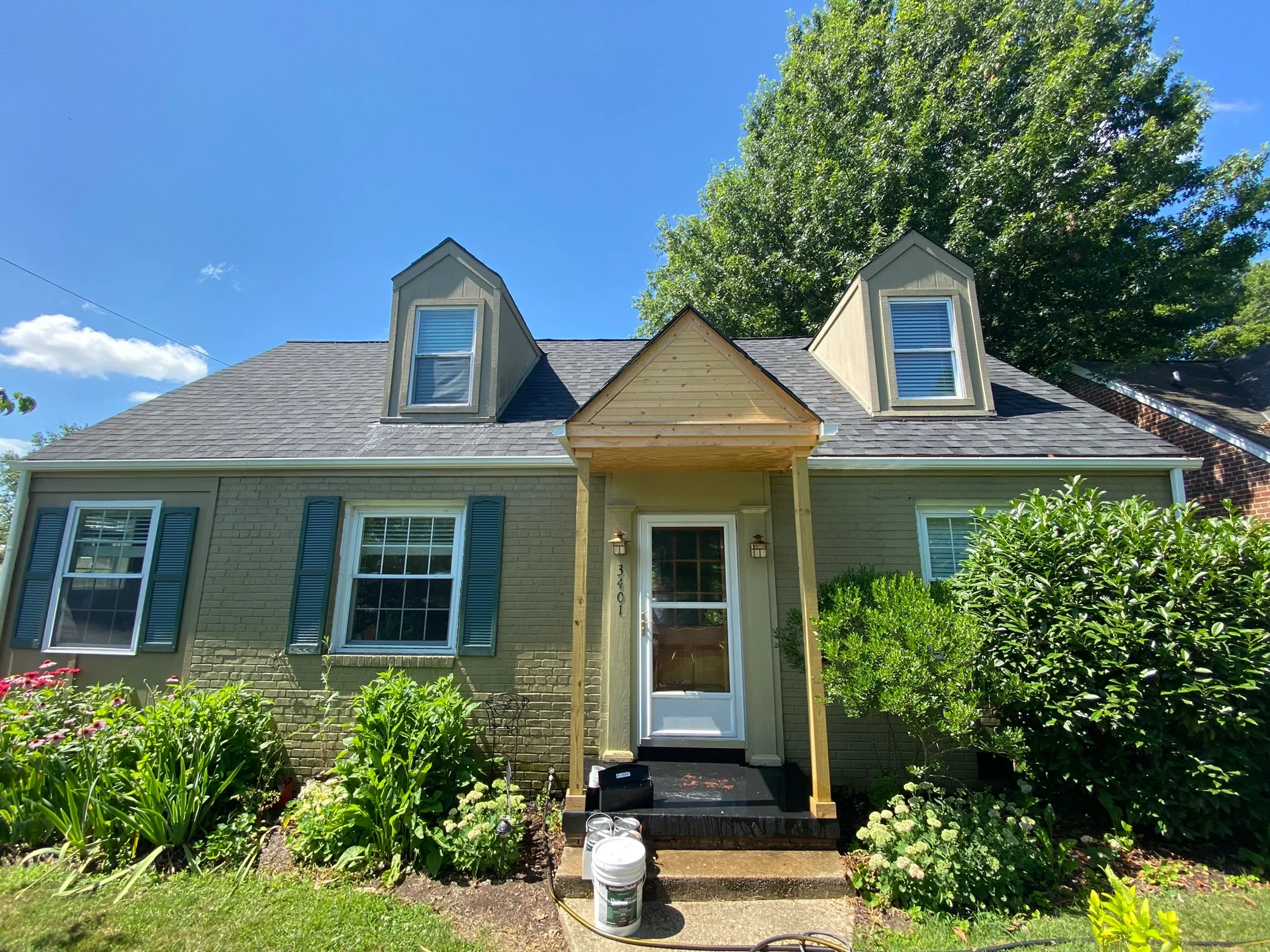 Sage green cottage with white trim, painted dormers, shutters, and entry portico