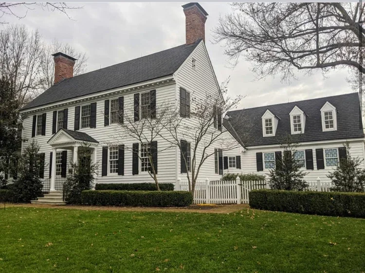 White painted colonial home with black shutters, brick chimneys, and white picket fence