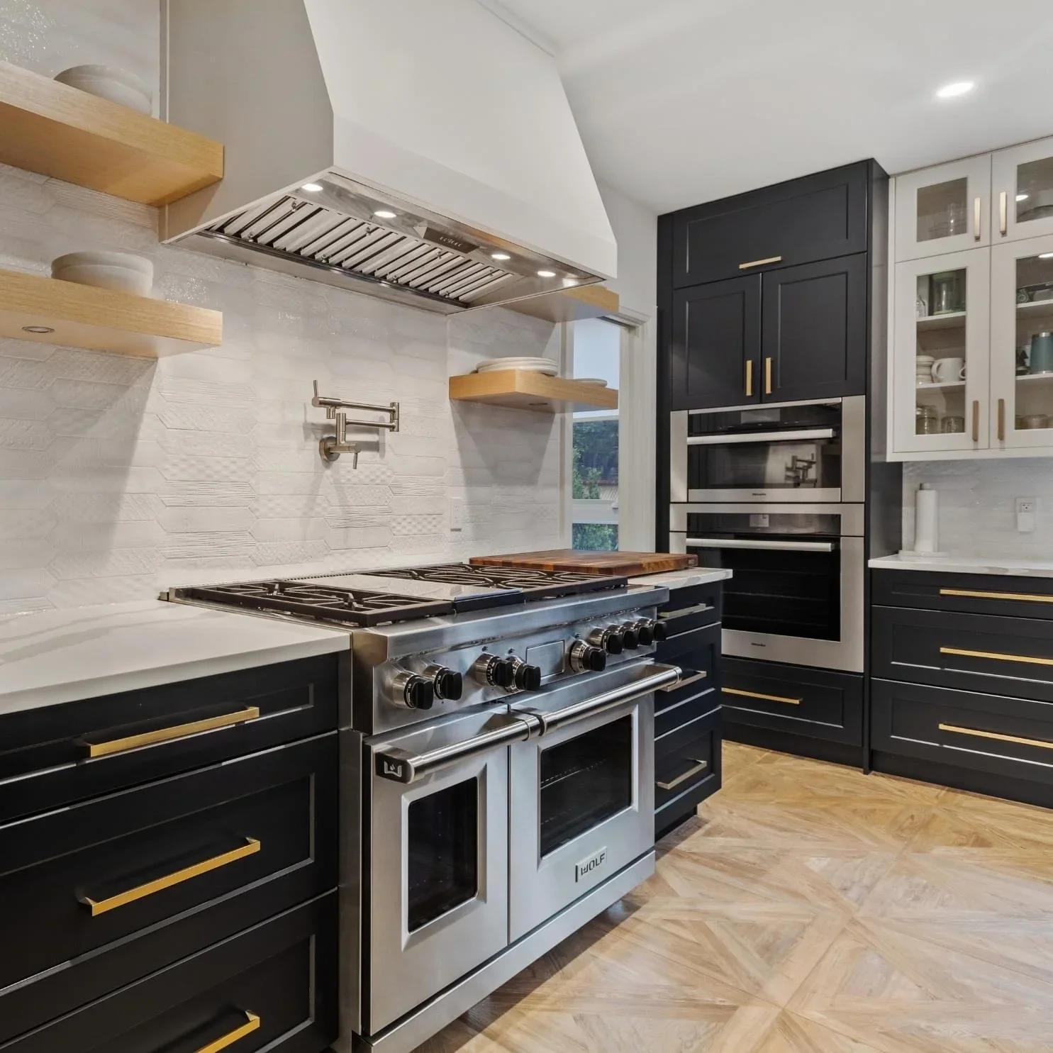 Black painted kitchen cabinets with gold handles, white painted walls, subway tile backsplash, and stainless steel range