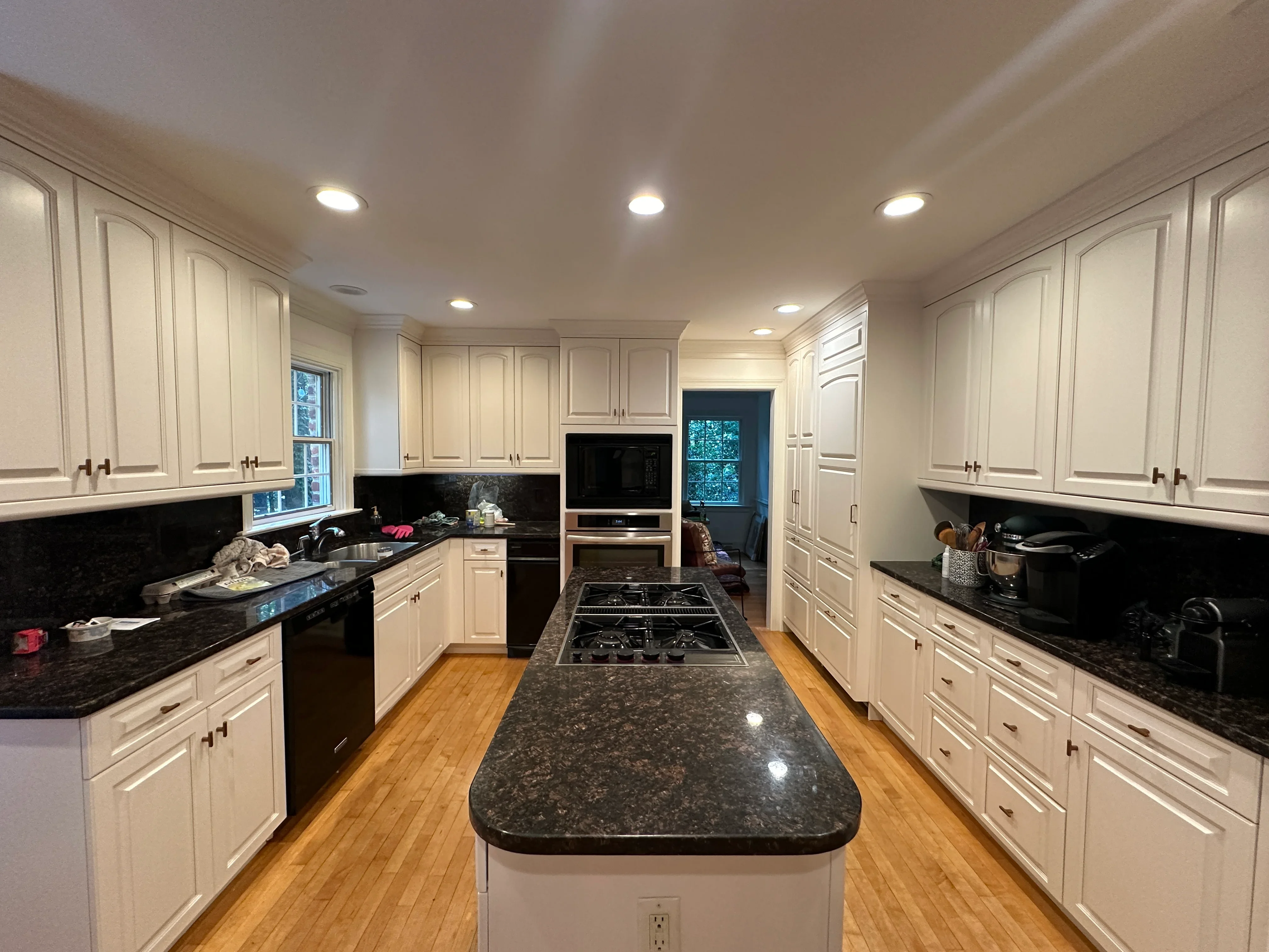 Cream painted kitchen cabinets with black granite counters, gas range, and recessed lighting