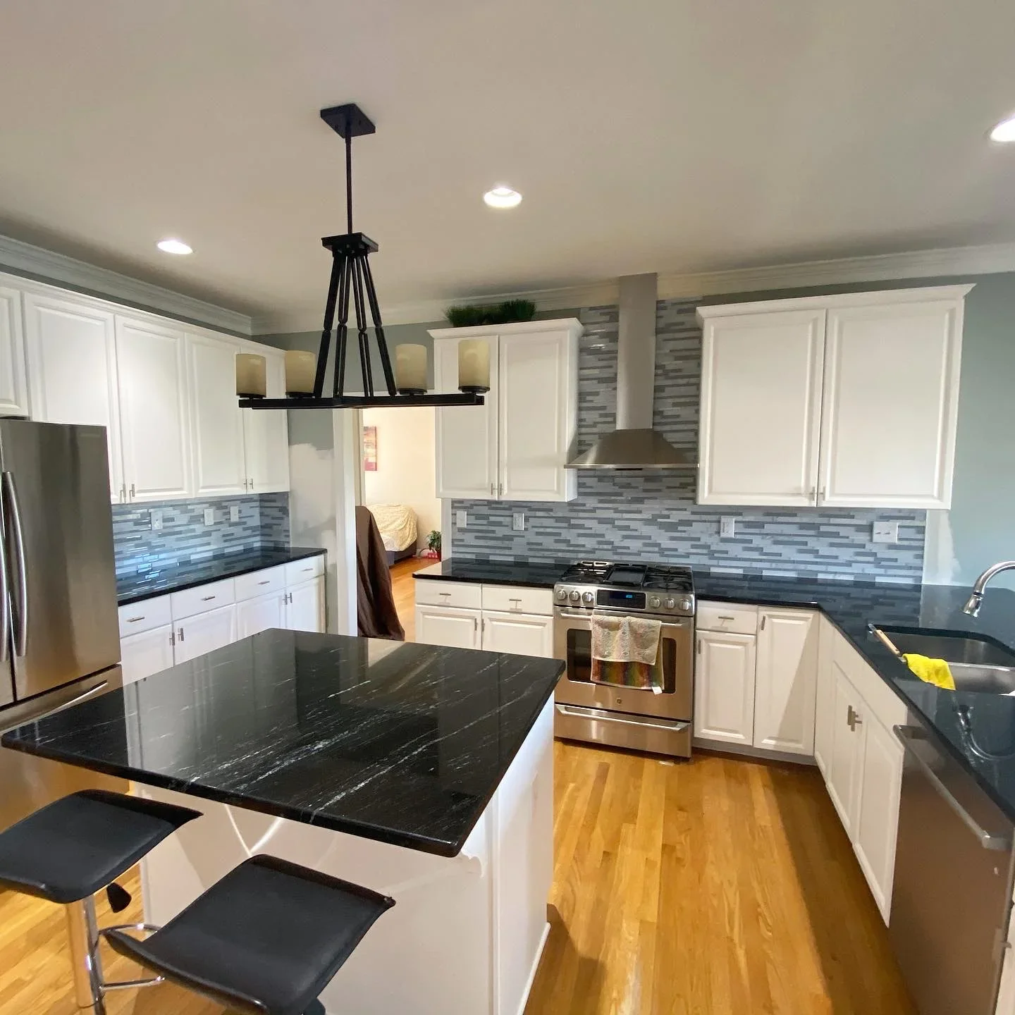 Kitchen with white painted cabinets, black marble countertops, blue tile backsplash, and freshly painted ceiling