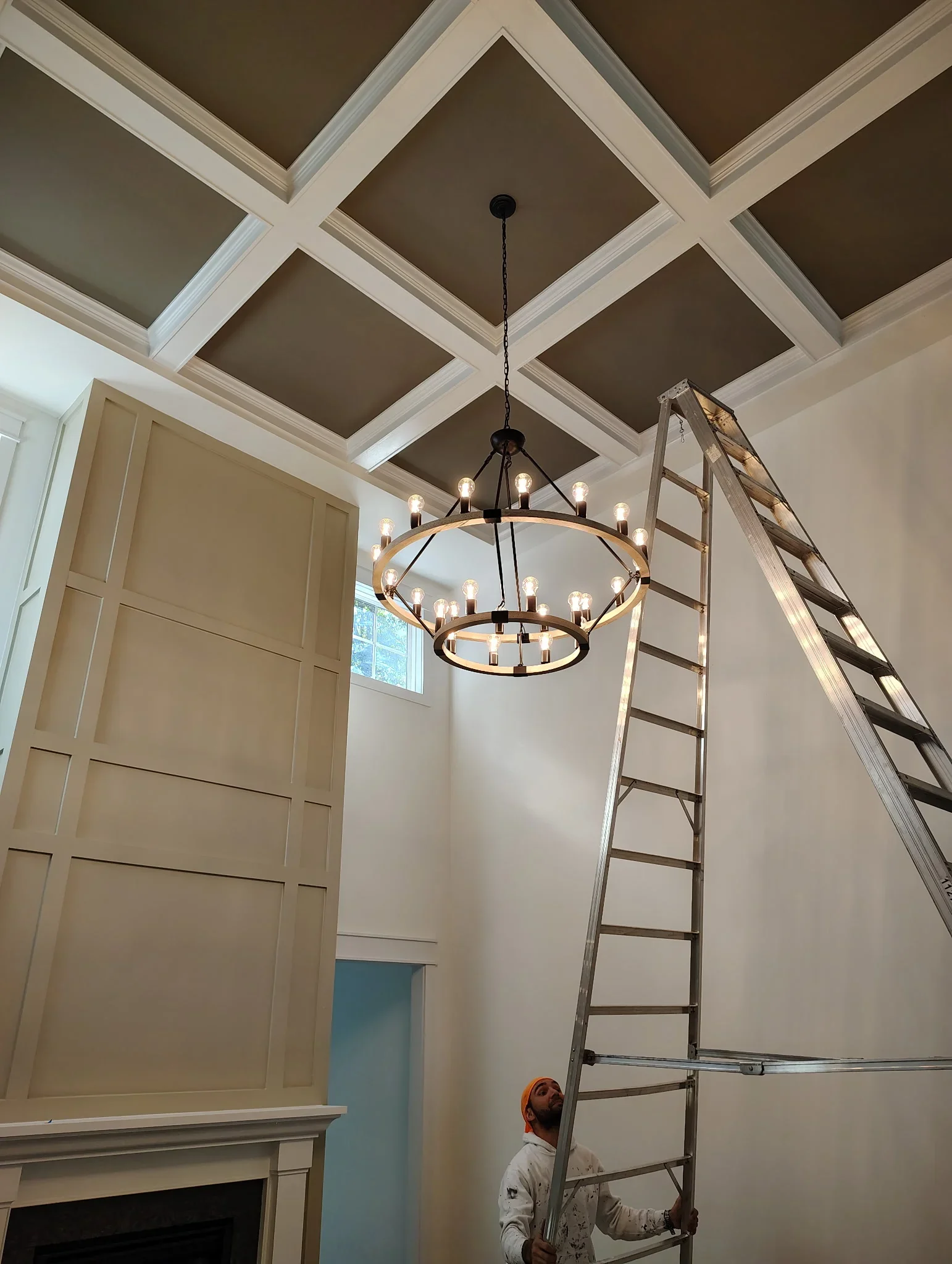Coffered ceiling with taupe and cream painted beams, black and brass chandelier installation