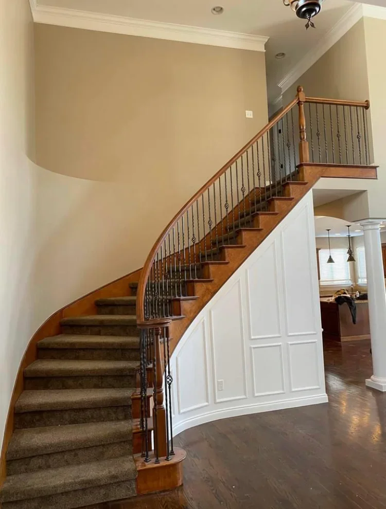Curved stairwell with beige walls, white ceiling, white trim, and wood railings with metal balusters