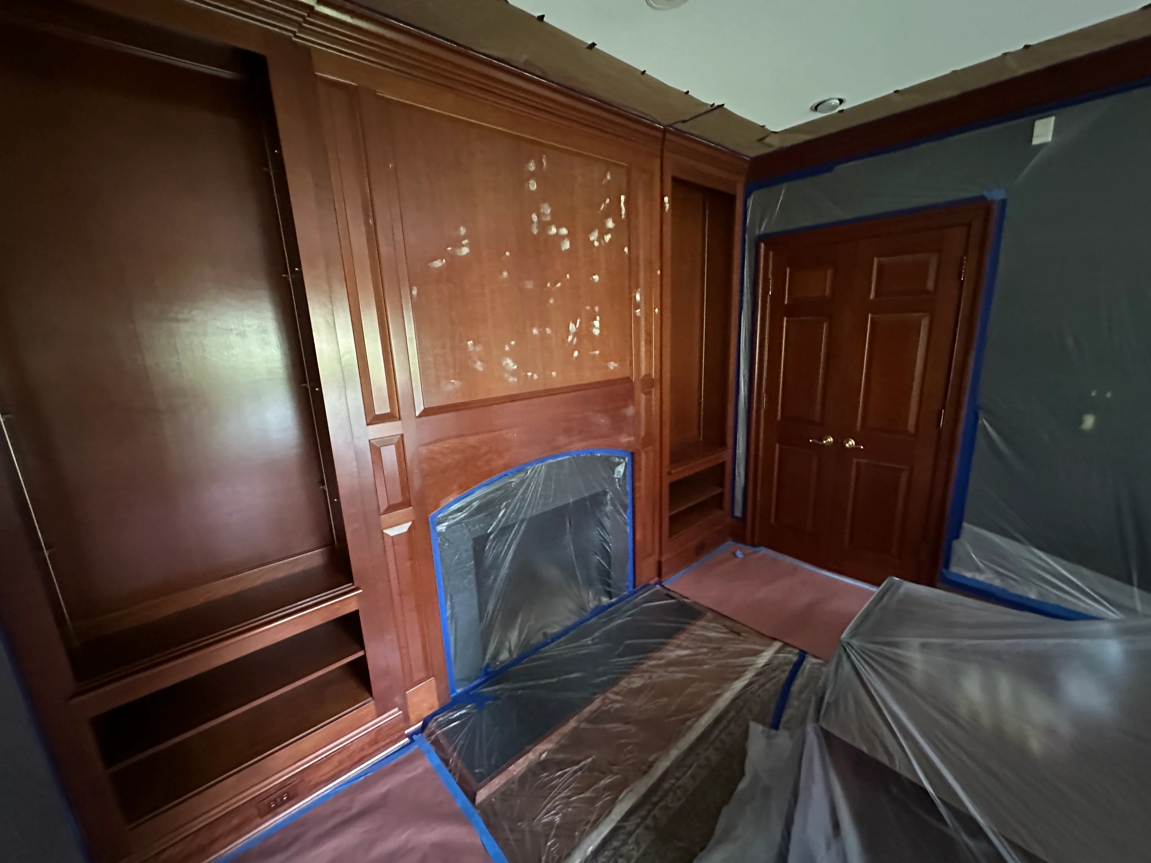 Interior room with wood paneling, six-panel doors, and plastic sheeting protecting surfaces during painting prep