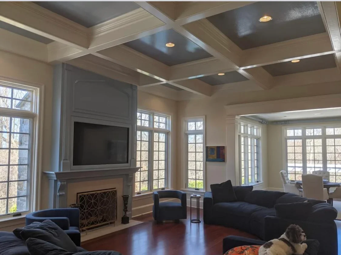 Coffered ceiling with recessed lights, white trim, and neutral painted walls in living room with fireplace