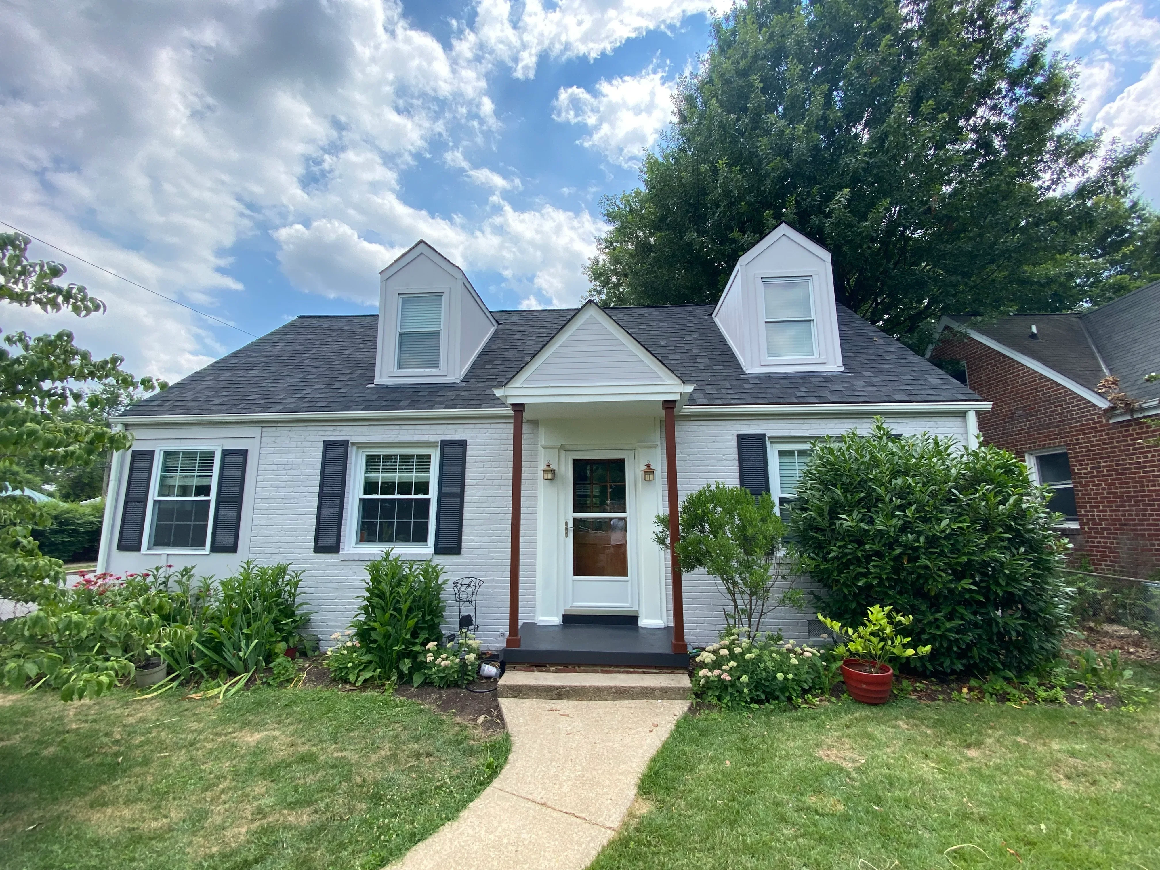 White painted house with gray roof, dormers, dark shutters, and brick entry columns
