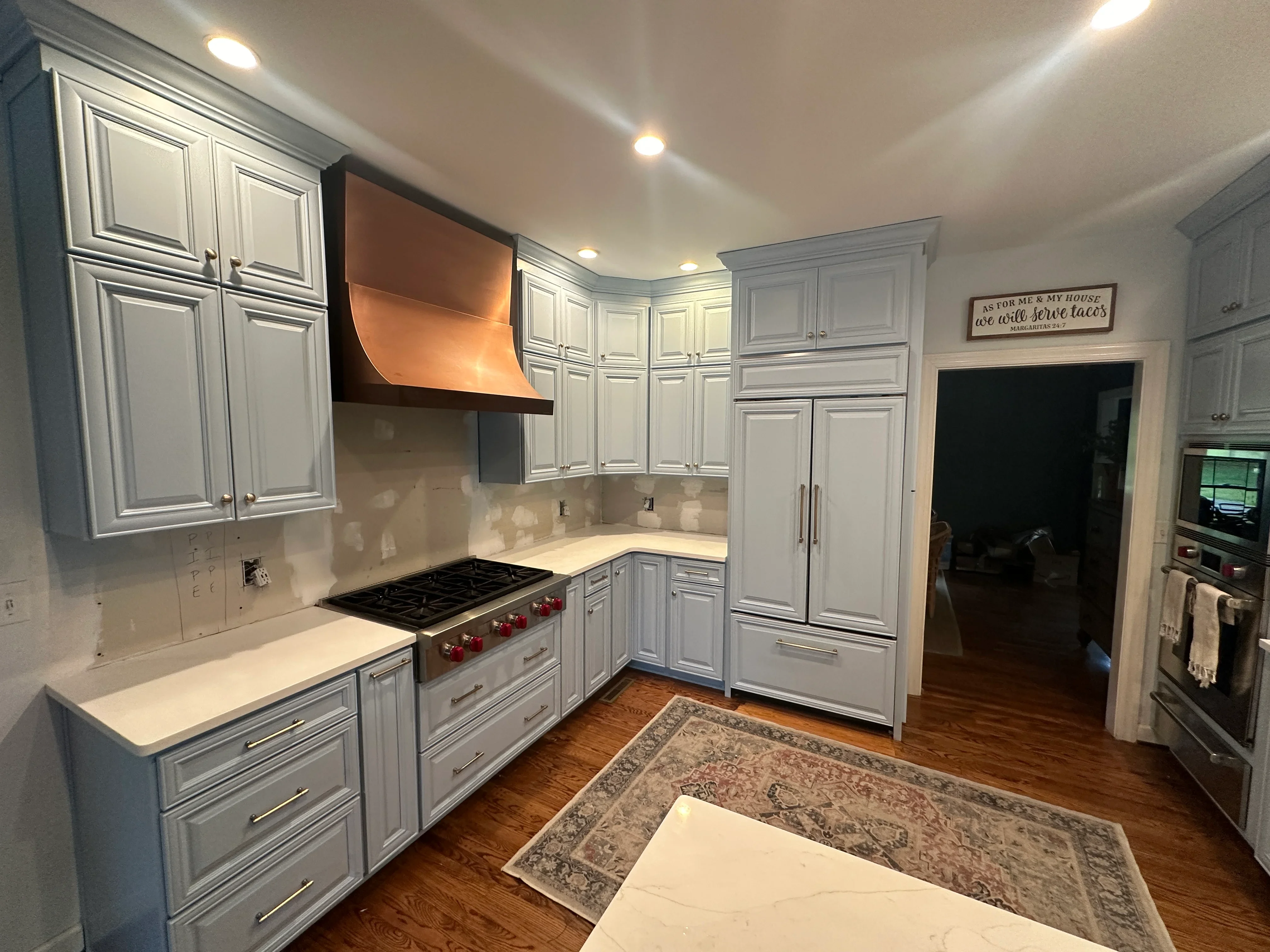 Gray-white painted kitchen cabinets with copper range hood, white countertops, and recessed lighting
