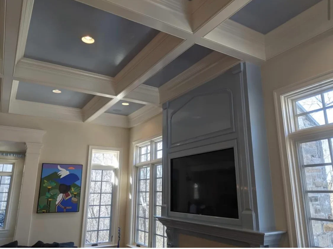 Coffered ceiling with cream and gray painted beams, recessed lights, and built-in TV cabinet