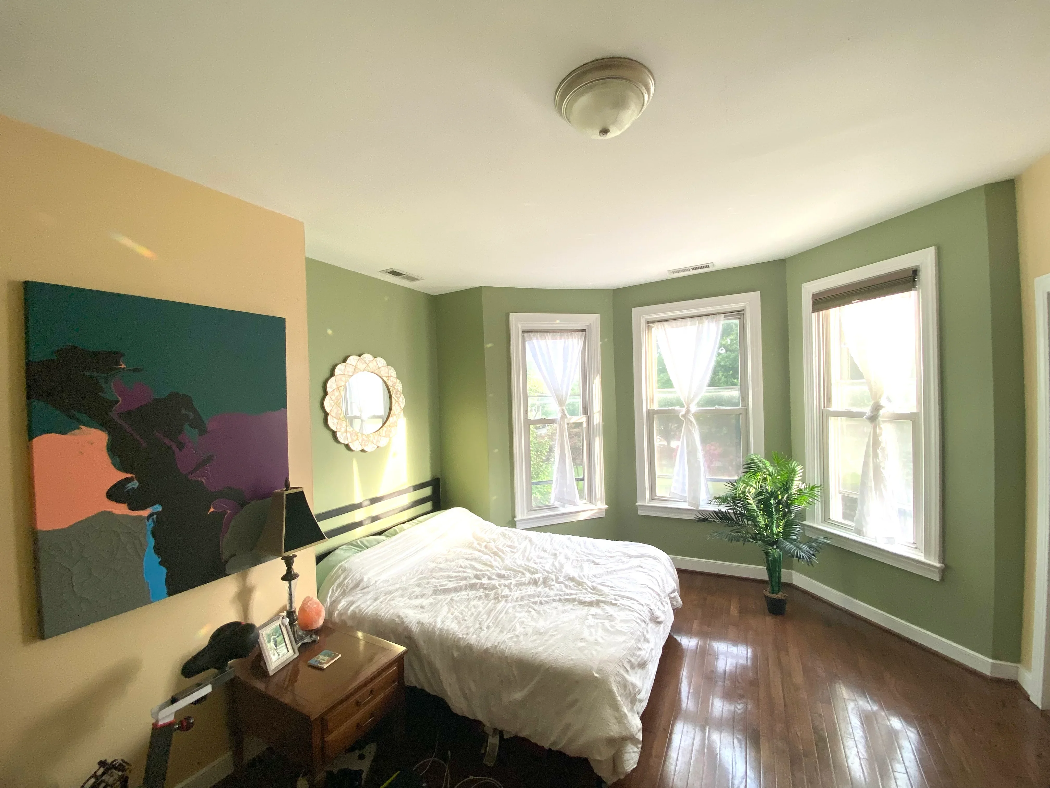 Bedroom with sage green walls, white trim, yellow accent wall, and hardwood flooring